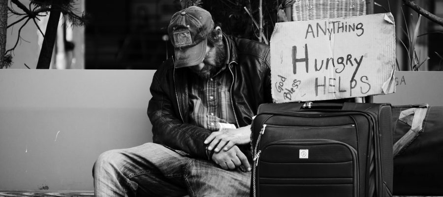 homeless man with his head down, sign that says "hungry, anything helps"