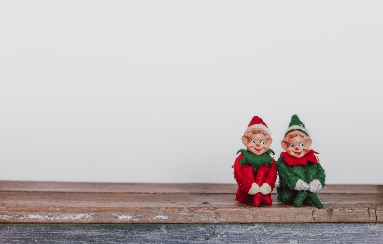 two elf figurines sitting in front of white wall, looking crazed