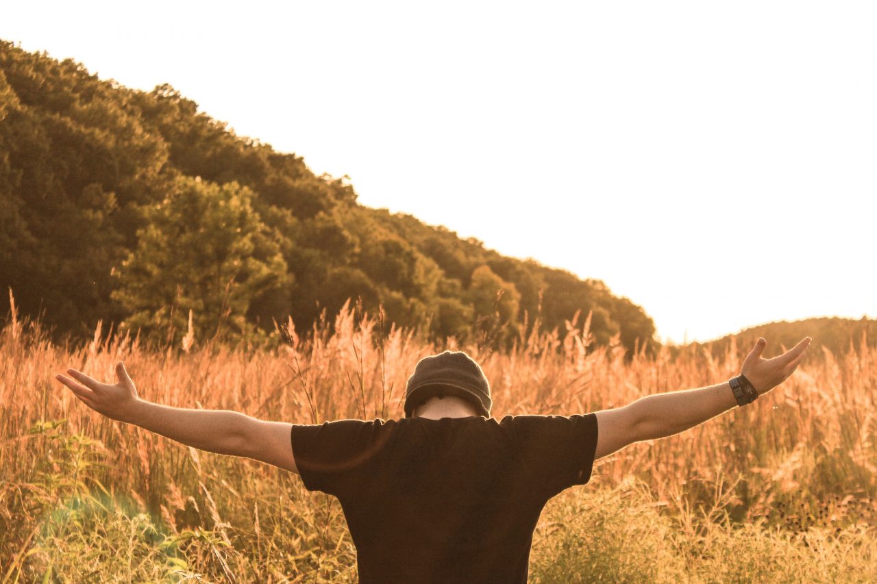 man standing in the middle of field, with his arms wide open.