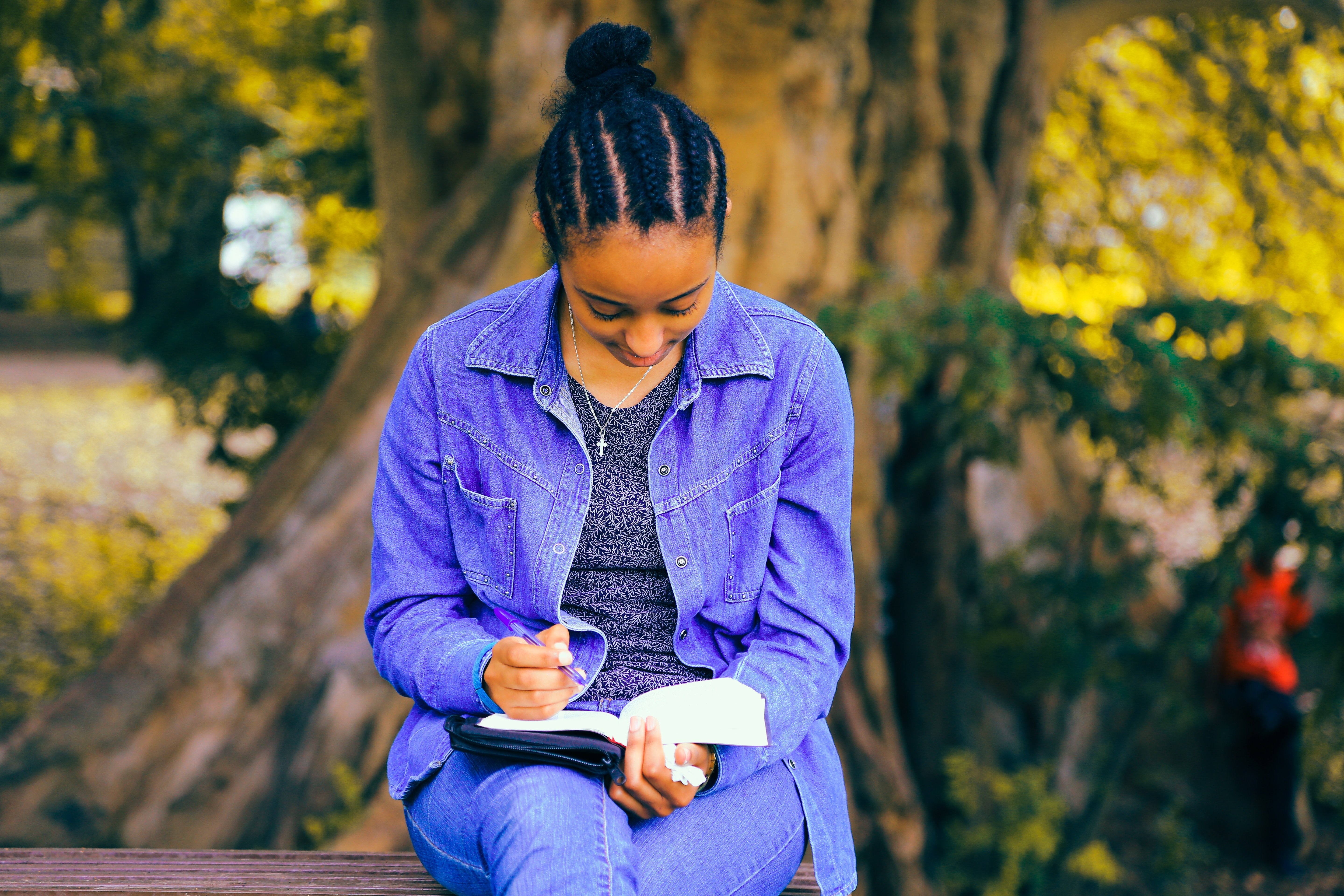Girl sitting outside, reading the bible while holding a pen