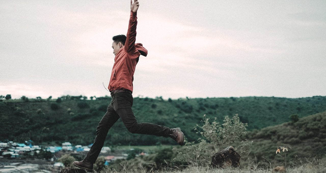 Man, on a field jumping to a rock.