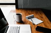 a laptop, coffee, notepad, and phone on a nice wooden desk