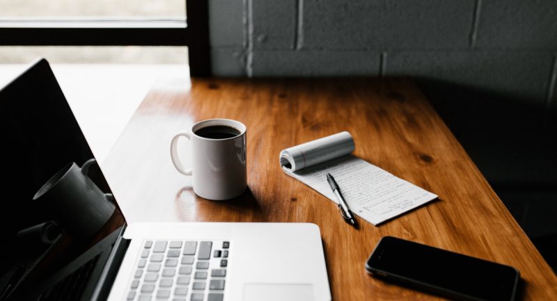 a laptop, coffee, notepad, and phone on a nice wooden desk